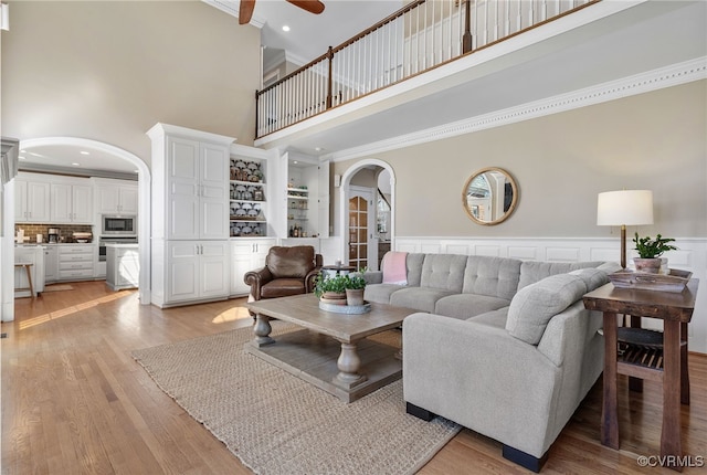 living room with crown molding, light hardwood / wood-style flooring, ceiling fan, and a high ceiling