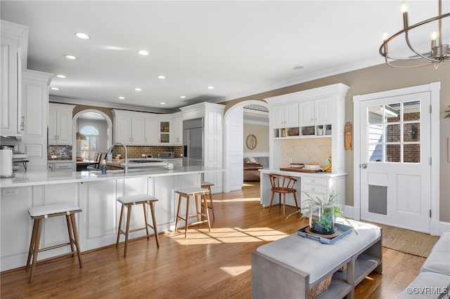 living room with crown molding, sink, an inviting chandelier, and light wood-type flooring