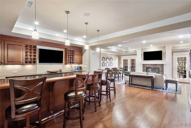 bar with crown molding, decorative light fixtures, a raised ceiling, and light wood-type flooring