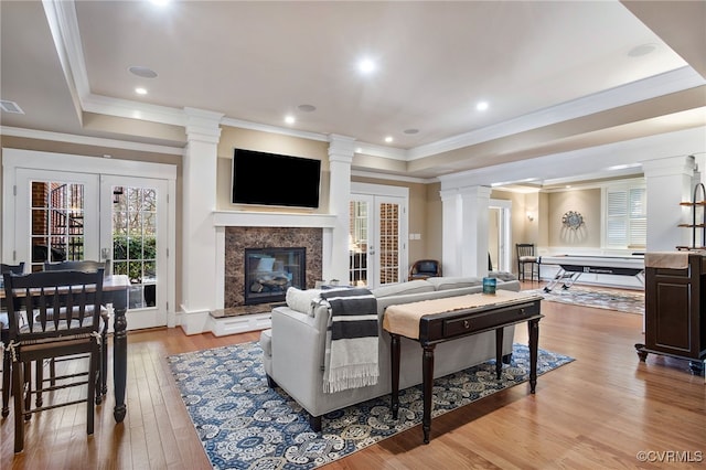 living room with decorative columns, a high end fireplace, light hardwood / wood-style floors, a raised ceiling, and french doors