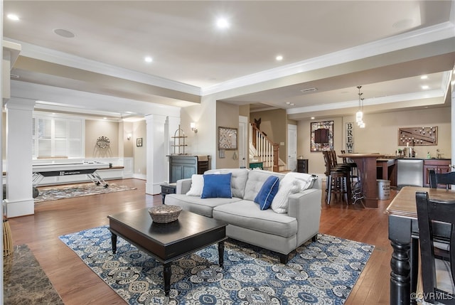 living room featuring decorative columns, ornamental molding, bar area, and dark hardwood / wood-style flooring