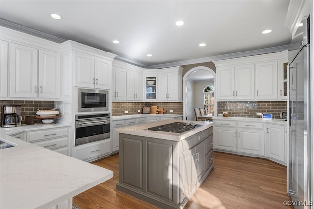 kitchen featuring white cabinetry, wood-type flooring, a center island, appliances with stainless steel finishes, and decorative backsplash