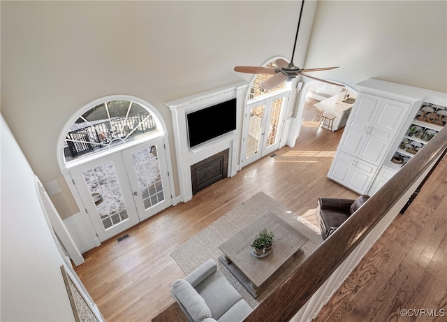 living room with a towering ceiling, french doors, ceiling fan, and light wood-type flooring