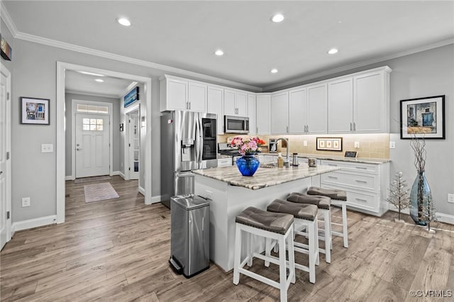 kitchen featuring stainless steel appliances, a sink, ornamental molding, light wood-type flooring, and decorative backsplash