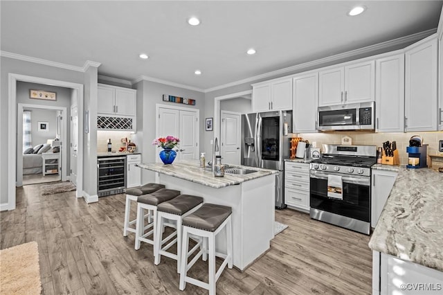 kitchen with beverage cooler, appliances with stainless steel finishes, a sink, and light wood-style flooring