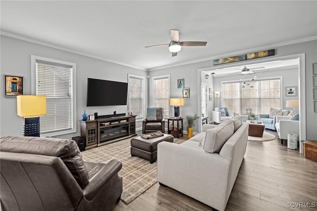 living area with ornamental molding, a glass covered fireplace, ceiling fan, and hardwood / wood-style floors