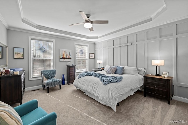 carpeted bedroom with a decorative wall, a ceiling fan, visible vents, ornamental molding, and a raised ceiling