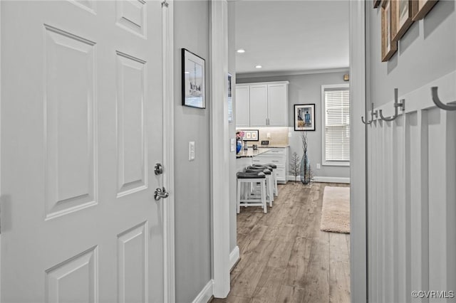 hallway featuring light wood-style floors, recessed lighting, crown molding, and baseboards