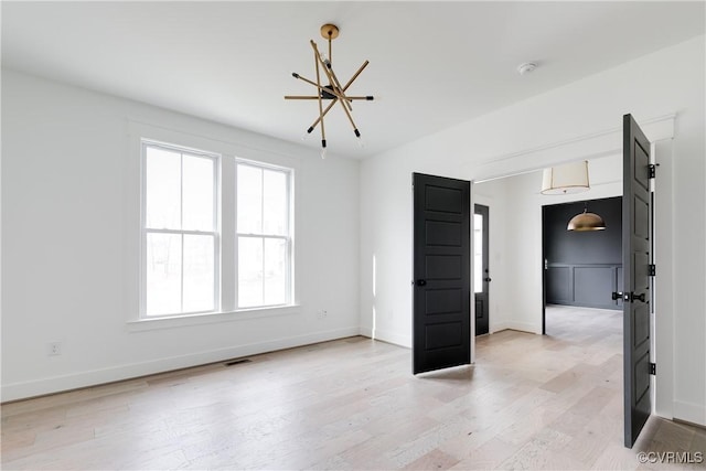 empty room with a chandelier and light wood-type flooring