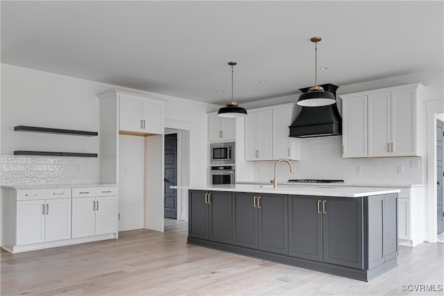 kitchen with pendant lighting, appliances with stainless steel finishes, white cabinetry, custom range hood, and a center island with sink