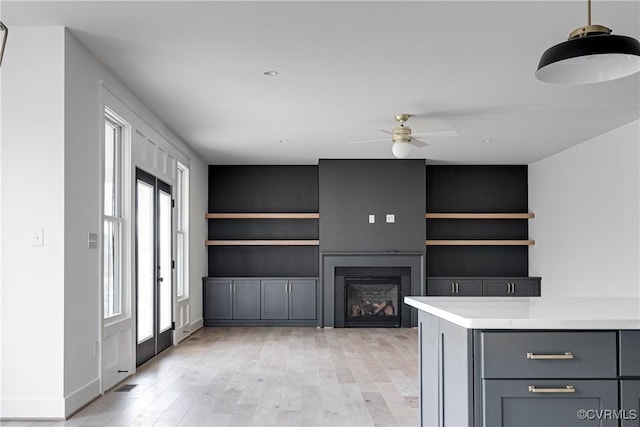 unfurnished living room featuring built in shelves, ceiling fan, and light wood-type flooring