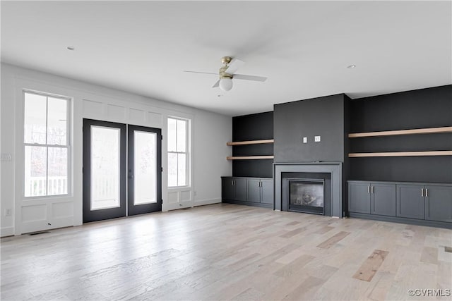 unfurnished living room featuring french doors, ceiling fan, built in shelves, and light wood-type flooring