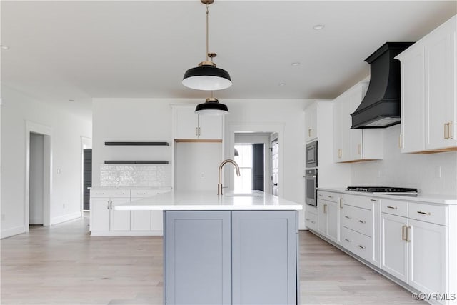 kitchen with pendant lighting, white cabinetry, custom exhaust hood, stainless steel appliances, and a center island with sink