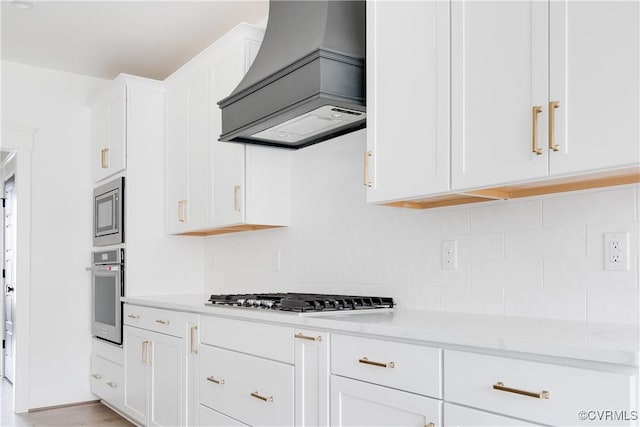 kitchen with custom exhaust hood, white cabinetry, light stone counters, and stainless steel appliances