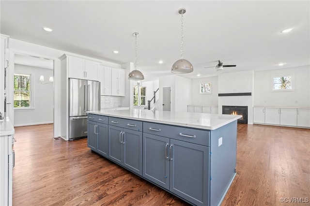 kitchen with tasteful backsplash, high end refrigerator, white cabinets, hanging light fixtures, and a center island