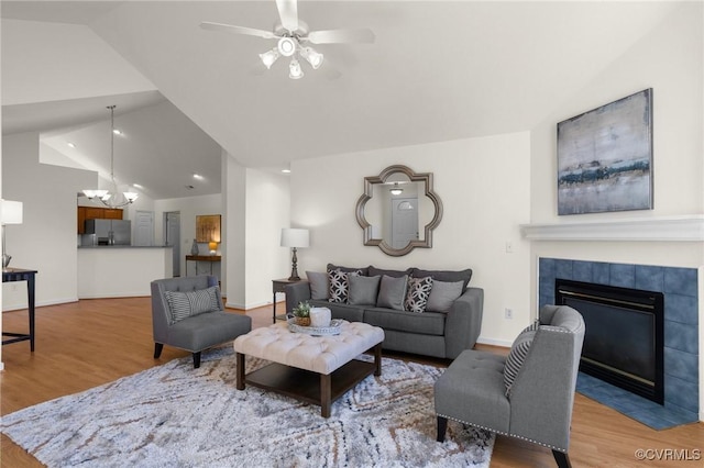 living room featuring lofted ceiling, ceiling fan with notable chandelier, a fireplace, and light hardwood / wood-style floors