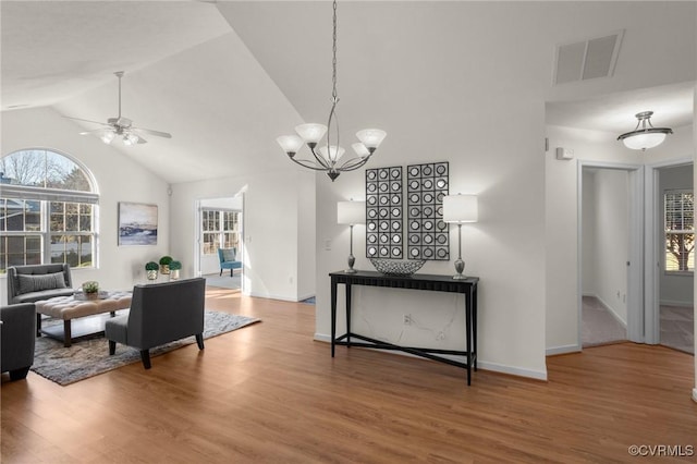 dining space featuring ceiling fan with notable chandelier, wood-type flooring, and high vaulted ceiling