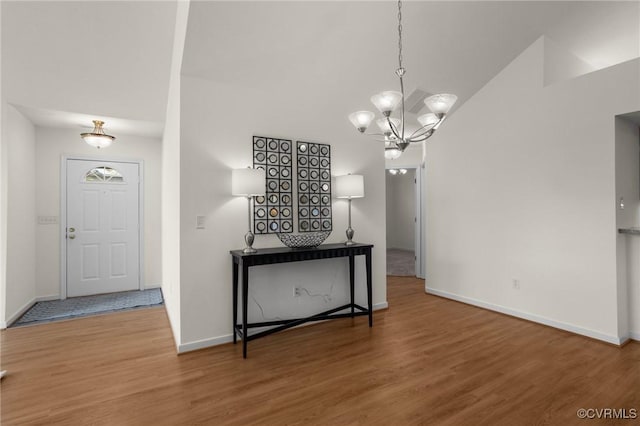 foyer entrance featuring an inviting chandelier, hardwood / wood-style floors, and vaulted ceiling