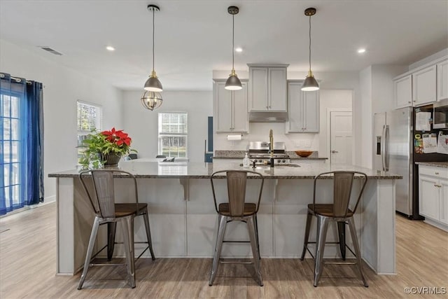 kitchen featuring visible vents, appliances with stainless steel finishes, a sink, under cabinet range hood, and a kitchen breakfast bar