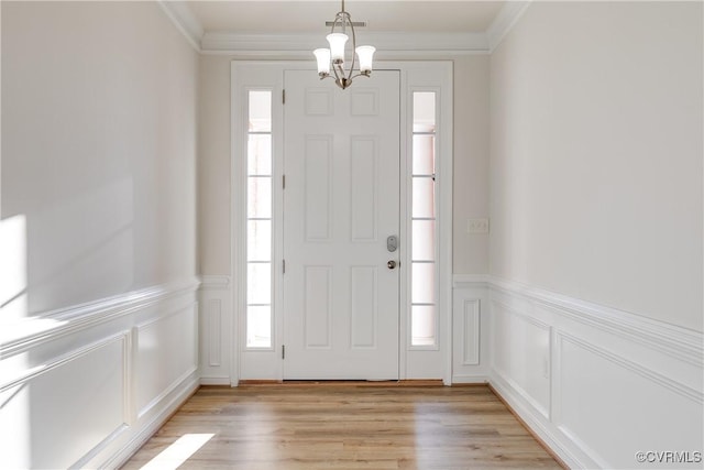 foyer entrance with an inviting chandelier, ornamental molding, and light hardwood / wood-style flooring