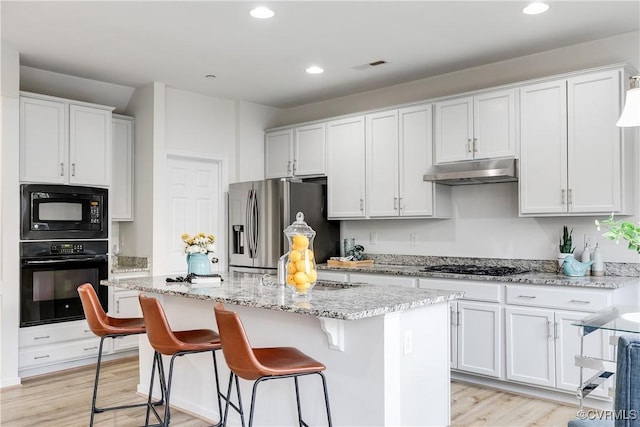 kitchen with a breakfast bar, a center island with sink, white cabinets, and black appliances