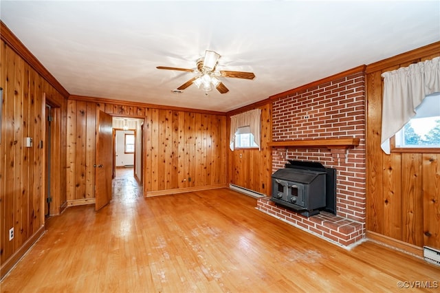 unfurnished living room with crown molding, a wood stove, a wealth of natural light, and baseboard heating