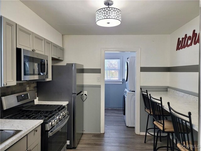 kitchen featuring stacked washer / drying machine, gray cabinetry, tasteful backsplash, dark hardwood / wood-style floors, and stainless steel appliances