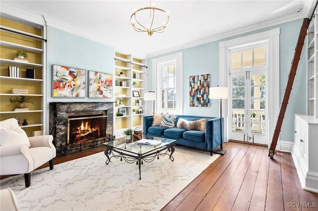 living area with hardwood / wood-style flooring, ornamental molding, a premium fireplace, an inviting chandelier, and built in shelves