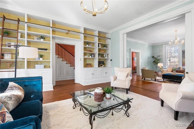 living room with hardwood / wood-style floors, built in shelves, ornamental molding, and a chandelier