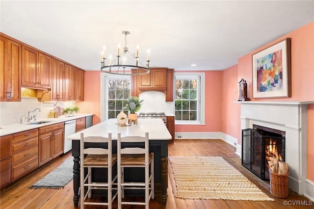 kitchen featuring decorative light fixtures, sink, a center island, stainless steel dishwasher, and light hardwood / wood-style floors