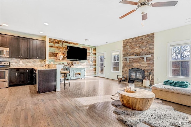 living room with ceiling fan, a stone fireplace, and light wood-type flooring