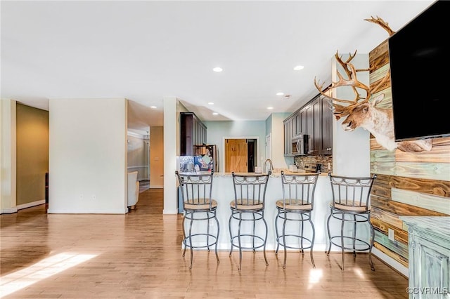 kitchen featuring dark brown cabinetry, light hardwood / wood-style flooring, a kitchen breakfast bar, kitchen peninsula, and stainless steel appliances