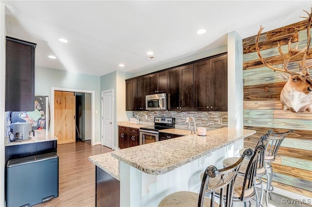 kitchen featuring stainless steel appliances, light hardwood / wood-style floors, light stone counters, and decorative backsplash