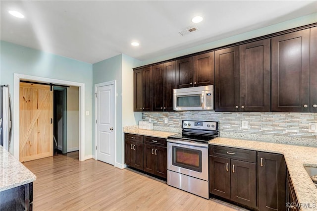 kitchen featuring stainless steel appliances, light stone countertops, a barn door, and dark brown cabinetry