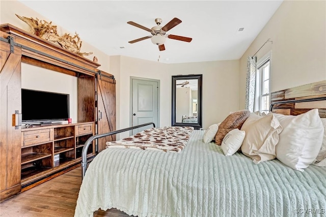 bedroom with hardwood / wood-style floors, a barn door, and ceiling fan