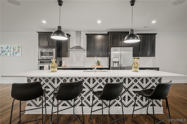 kitchen with a spacious island, appliances with stainless steel finishes, hanging light fixtures, and wall chimney range hood