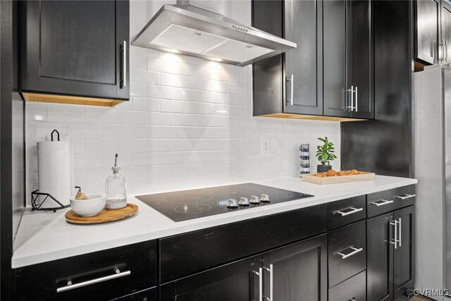 kitchen featuring tasteful backsplash, stainless steel refrigerator, black electric stovetop, and wall chimney range hood