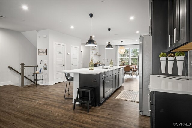 kitchen featuring sink, a breakfast bar area, stainless steel fridge, an island with sink, and decorative light fixtures