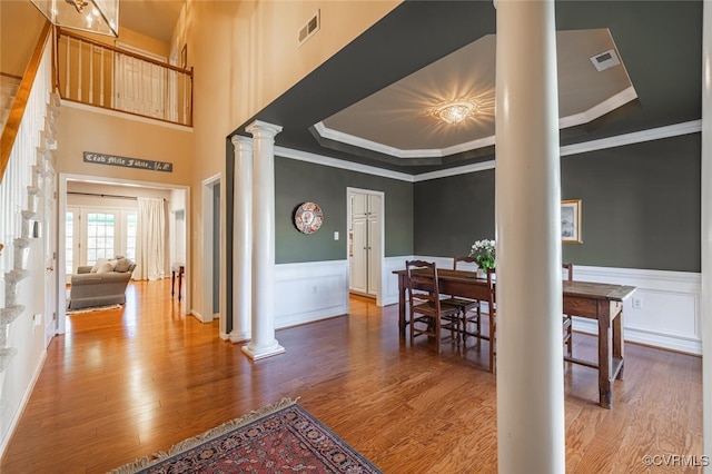 dining space with ornamental molding, a raised ceiling, decorative columns, and wood-type flooring