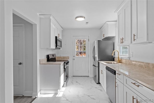 kitchen with white cabinetry, stainless steel appliances, light stone countertops, and sink