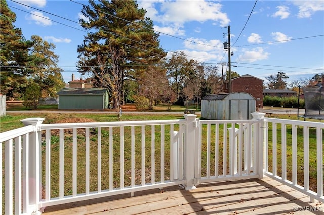 wooden terrace with a trampoline, a lawn, and a storage unit