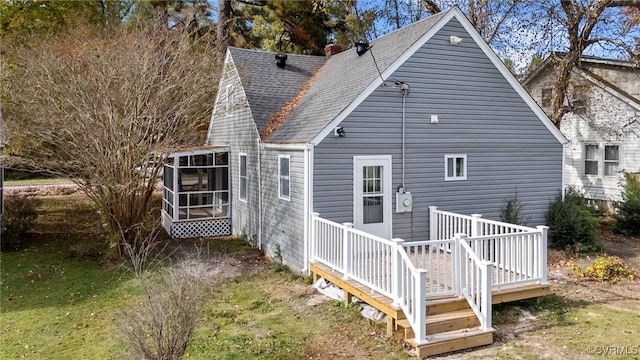 back of property featuring a wooden deck, a lawn, and a sunroom