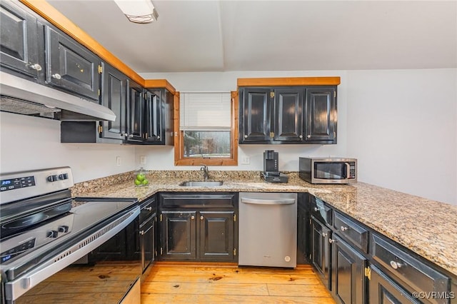 kitchen with appliances with stainless steel finishes, sink, light stone counters, and light wood-type flooring