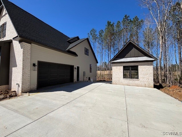 view of side of home with a garage, brick siding, concrete driveway, and roof with shingles