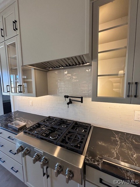 kitchen featuring dark stone countertops, glass insert cabinets, stainless steel gas stovetop, backsplash, and premium range hood