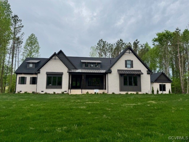 back of house with a lawn, a standing seam roof, metal roof, and brick siding