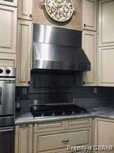 kitchen featuring multiple ovens, wall chimney exhaust hood, stainless steel gas stovetop, and cream cabinetry