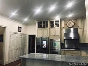 kitchen featuring dark stone countertops, stainless steel appliances, cream cabinetry, and wall chimney exhaust hood