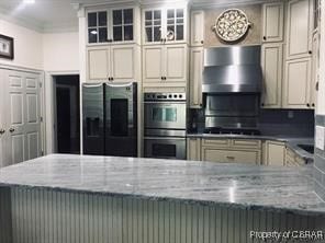 kitchen with light stone counters, cream cabinetry, appliances with stainless steel finishes, and wall chimney range hood