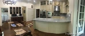 kitchen featuring wall chimney exhaust hood, an inviting chandelier, stainless steel fridge with ice dispenser, kitchen peninsula, and white cabinets